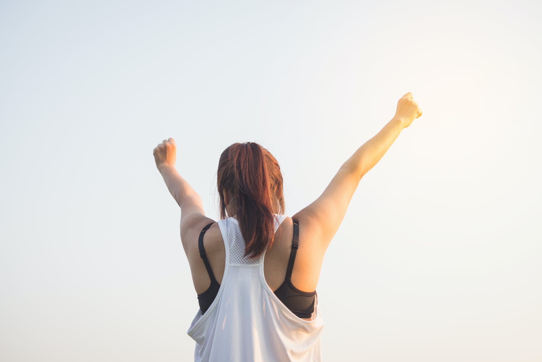 Woman wearing black bra and white tank top raising both hands on top fitness meets nutrition