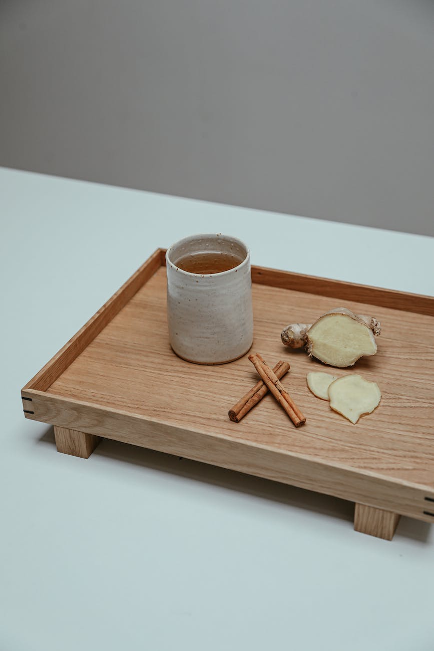 Ceramic mug on wooden tray with ginger and cinnamon sticks morning beverages
